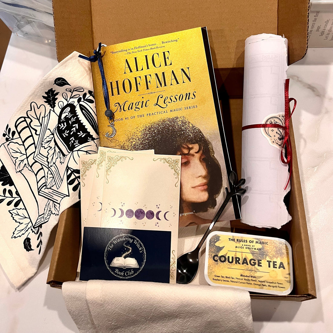 A curated Wandering Witch Book Club box featuring Magic Lessons by Alice Hoffman, Courage Tea, ritual cards, a scroll, and a moon phase card